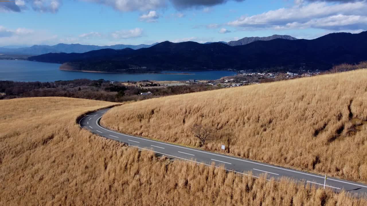 蜿蜒的道路穿过金色的田野，背景是湖泊和山脉，鸟瞰视频素材