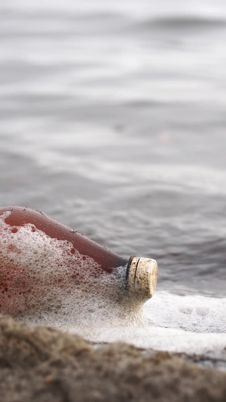 环境污染的概念。一个塑料瓶在湖边。垂直视频，特写视频下载