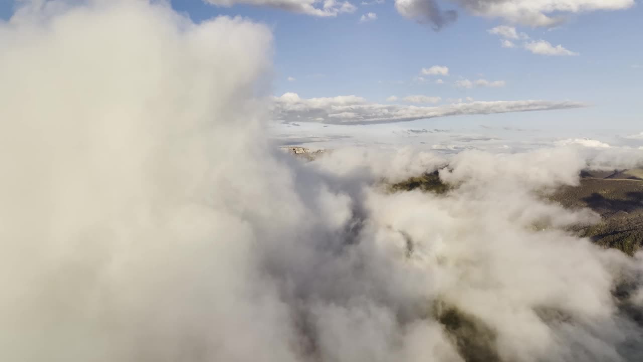 鸟瞰在群山中蓬松的云层之间飞行，在夕阳的光线下欣赏岩石高原的壮丽景色。在云中飞翔视频素材