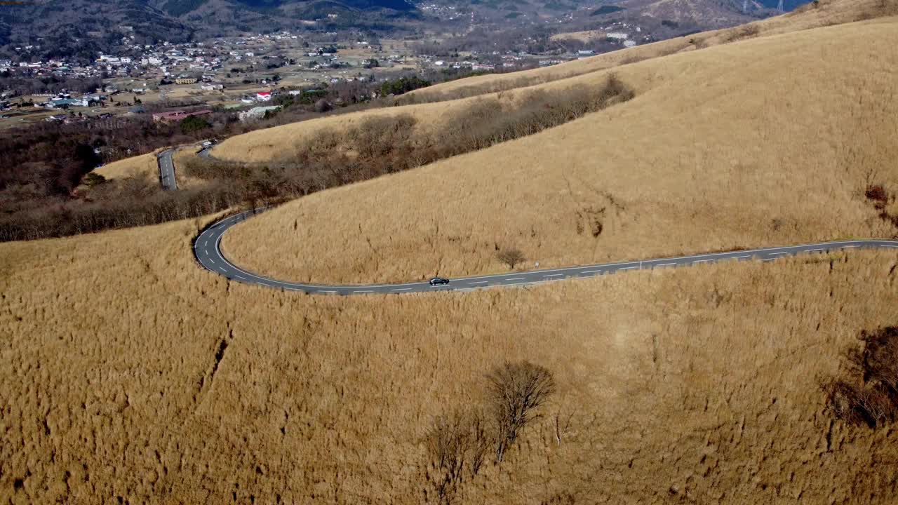 一辆孤独的汽车行驶在蜿蜒的道路上，穿过金色的草山，没有树木，阳光，鸟瞰视频素材