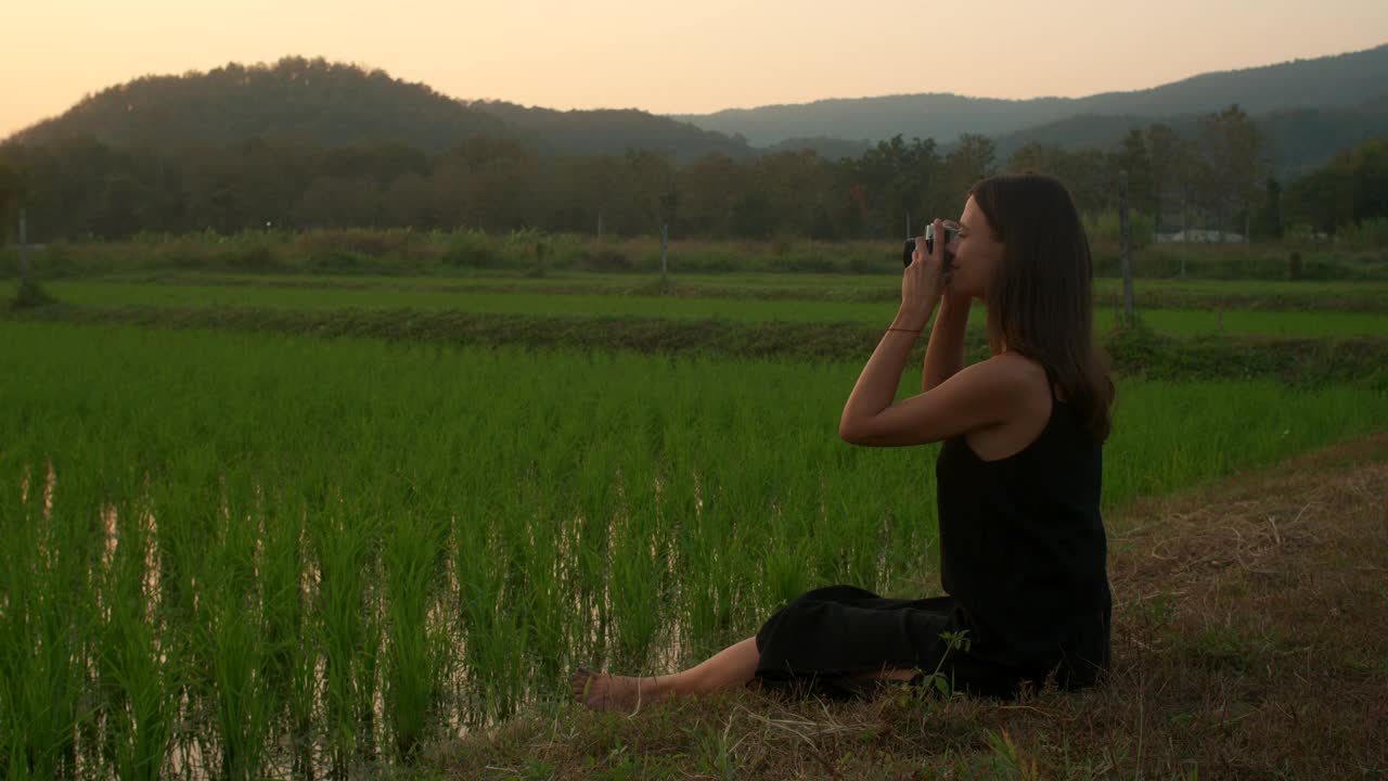 年轻女子在夕阳下拍摄稻田的照片视频素材