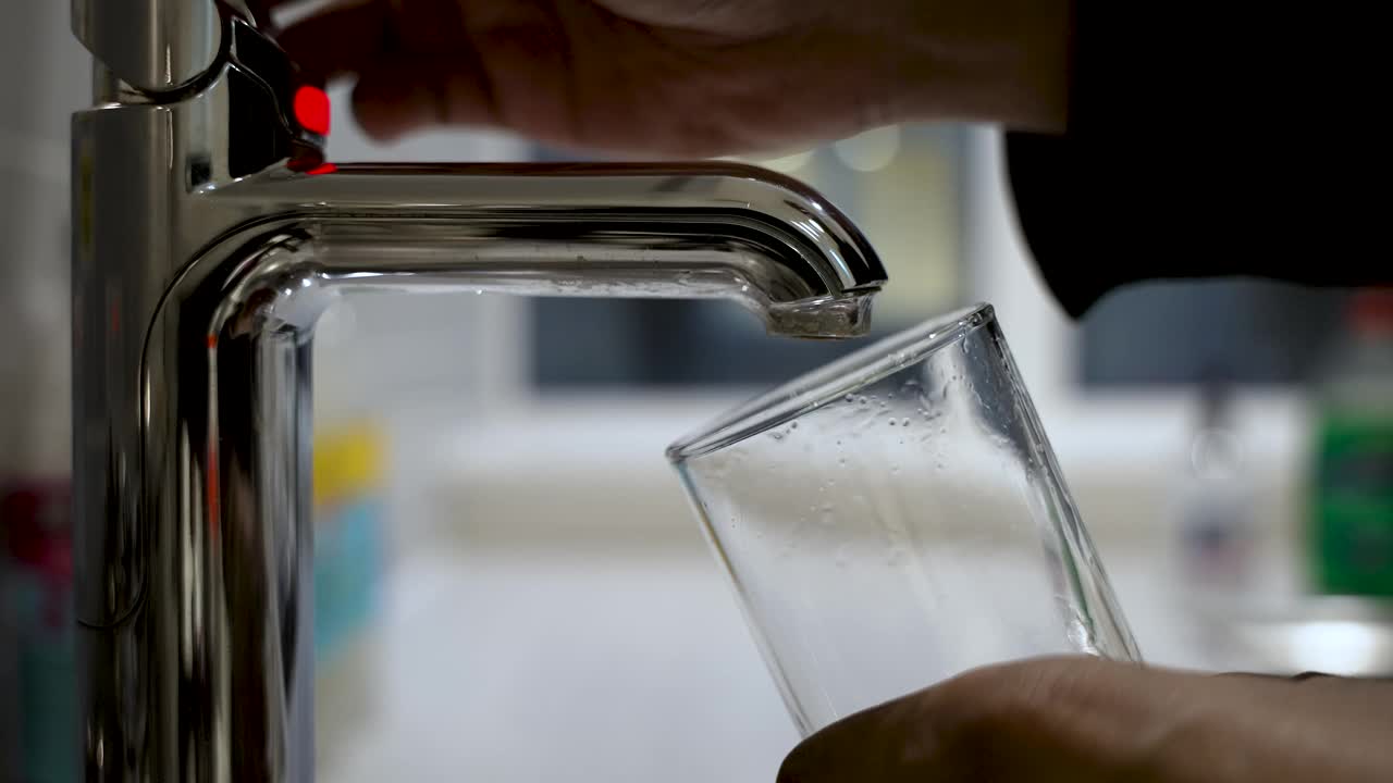 厨房里一只手从现代水龙头里往玻璃杯里注水的特写视频素材