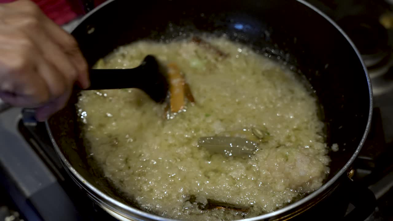 用勺子搅拌锅里的洋葱和肉桂棒，唤起烹饪的精髓和细致的食物准备。慢动作视频素材