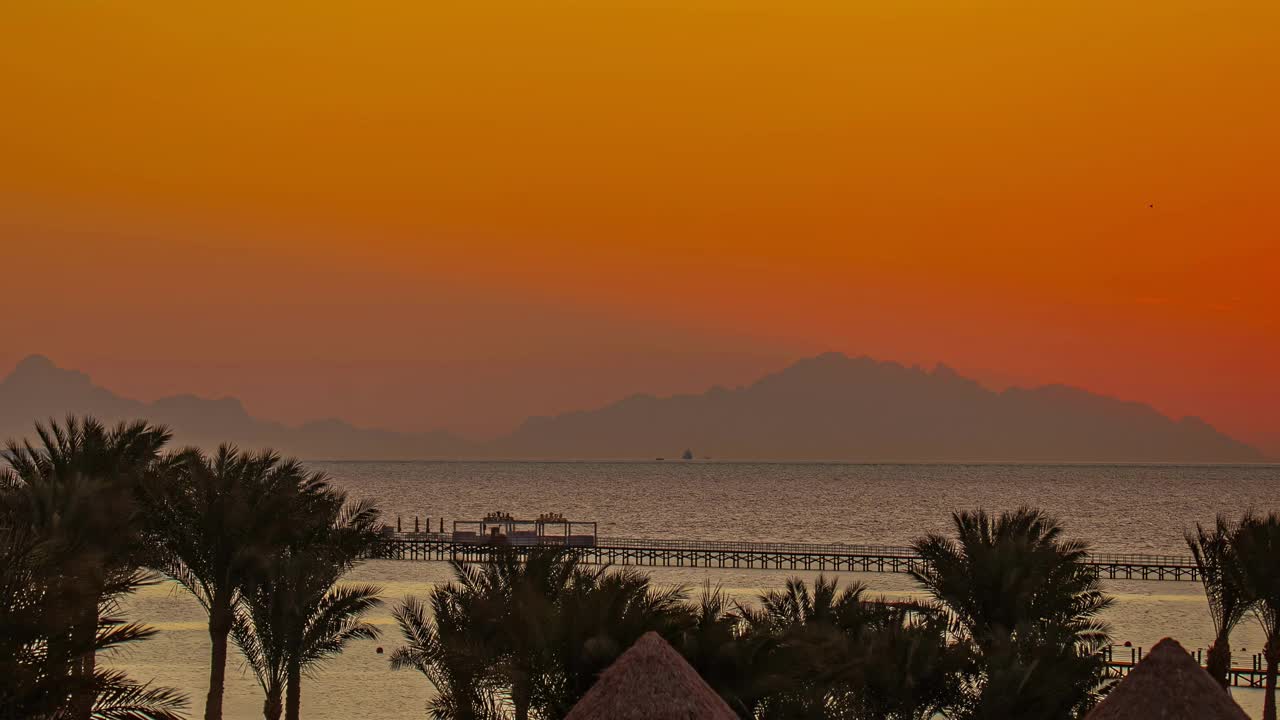 橘黄色的夕阳映在宁静的海面上，棕榈树和码头的剪影随着时间流逝视频素材