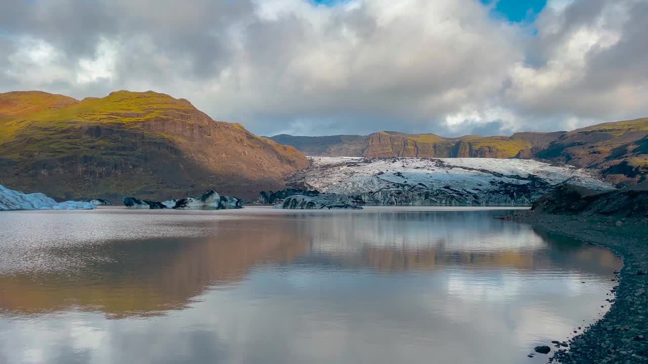 阳光照耀下的Sólheimajökull冰岛冰川反射在宁静的湖泊中，与戏剧性的天空视频素材