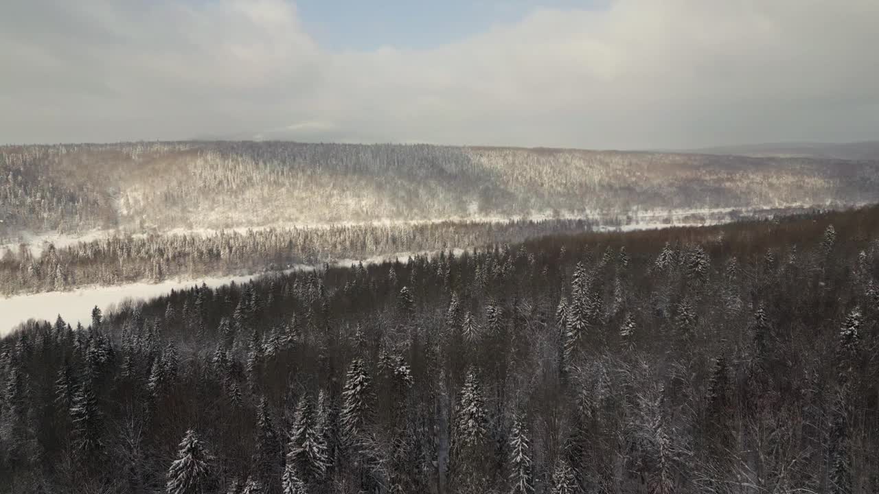 俯瞰美丽的冬季景观，有山丘和森林。夹。美丽的地平线，冬季森林的全景和多云的天空。冬季景观，森林和阳光透过多云的天空视频素材