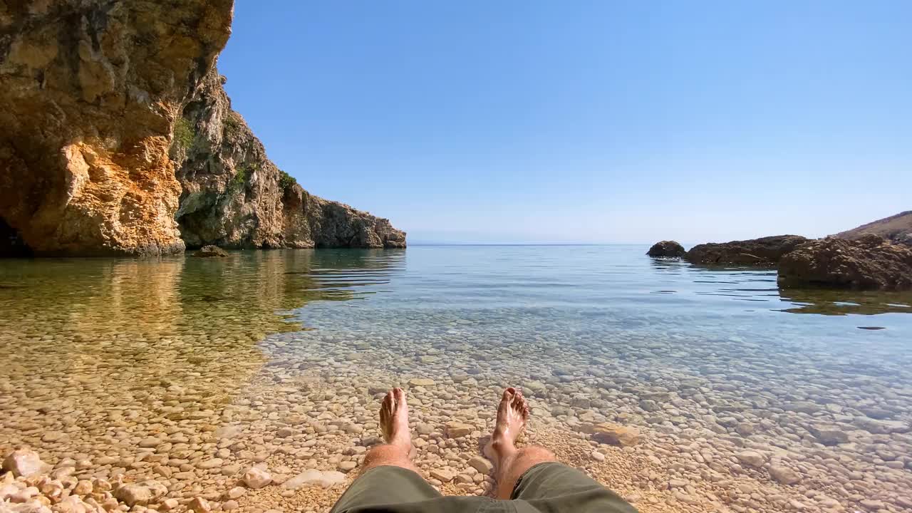 个人视角，一个男人享受宁静的海滩时间，他的腿在海里视频素材