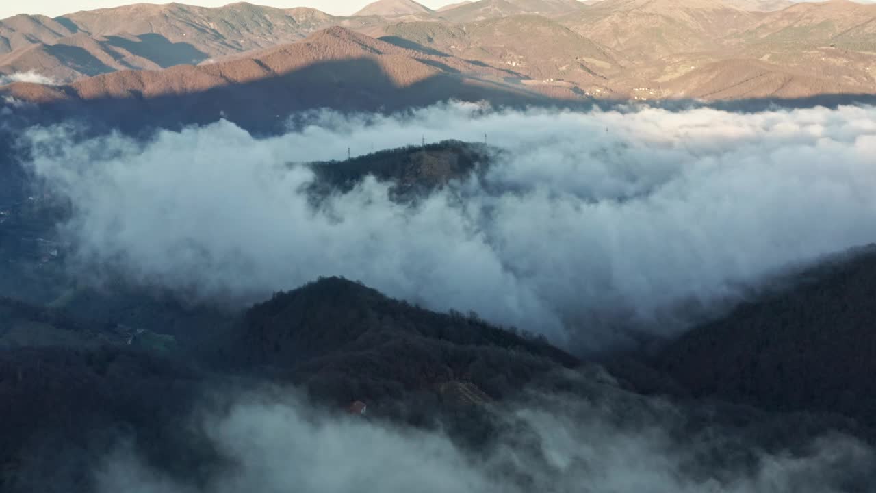 朦胧的山峰从浓密的云层中浮现出来，从黎明的空中视角拍摄视频素材