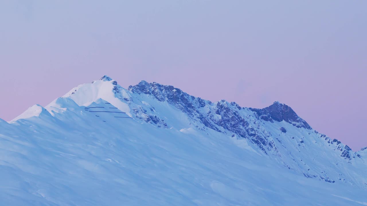 通过这段令人着迷的无人机镜头，见证日出在白雪皑皑的山脉剪影上的空灵魅力。粉色的天空视频素材