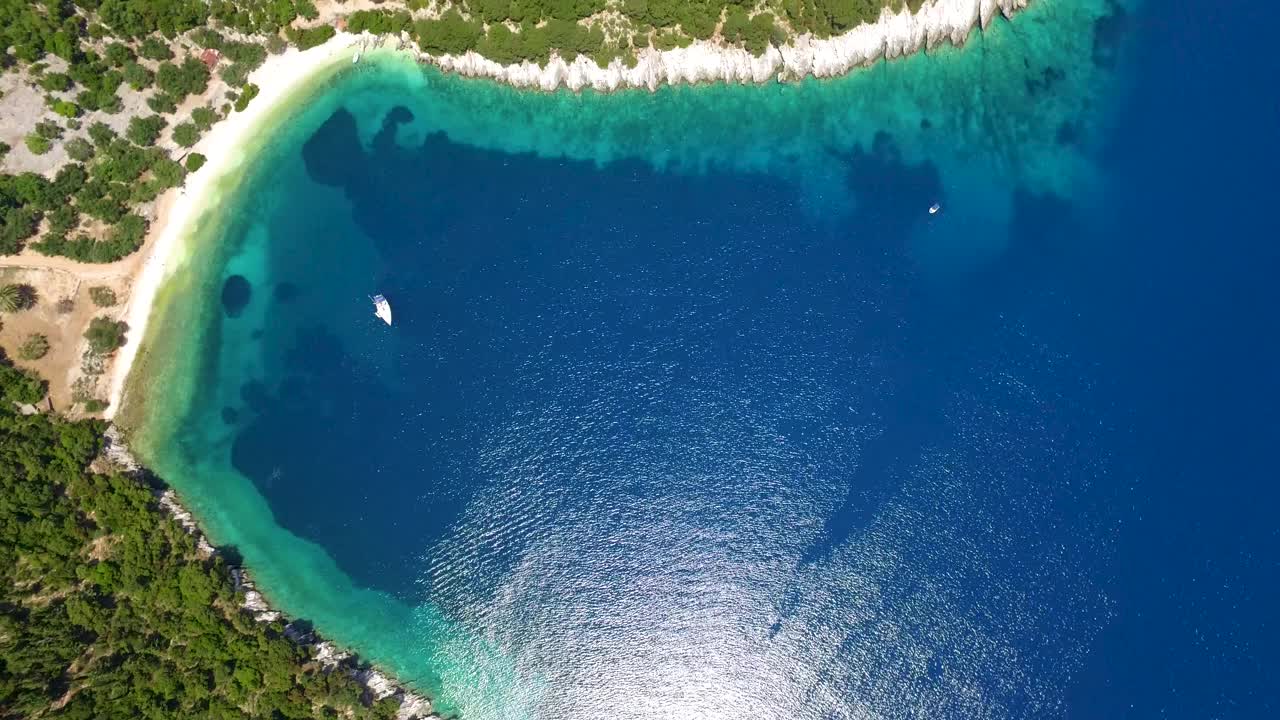 水晶蓝色的海水边缘郁郁葱葱的绿色海湾在凯法利尼亚岛，鸟瞰图，阳光明媚的一天视频素材