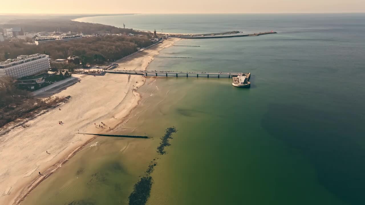 体验宁静的美丽Kołobrzeg码头在一个阳光明媚的冬日。平静的大海，晴朗的天空，游客悠闲地沿着码头散步。视频下载