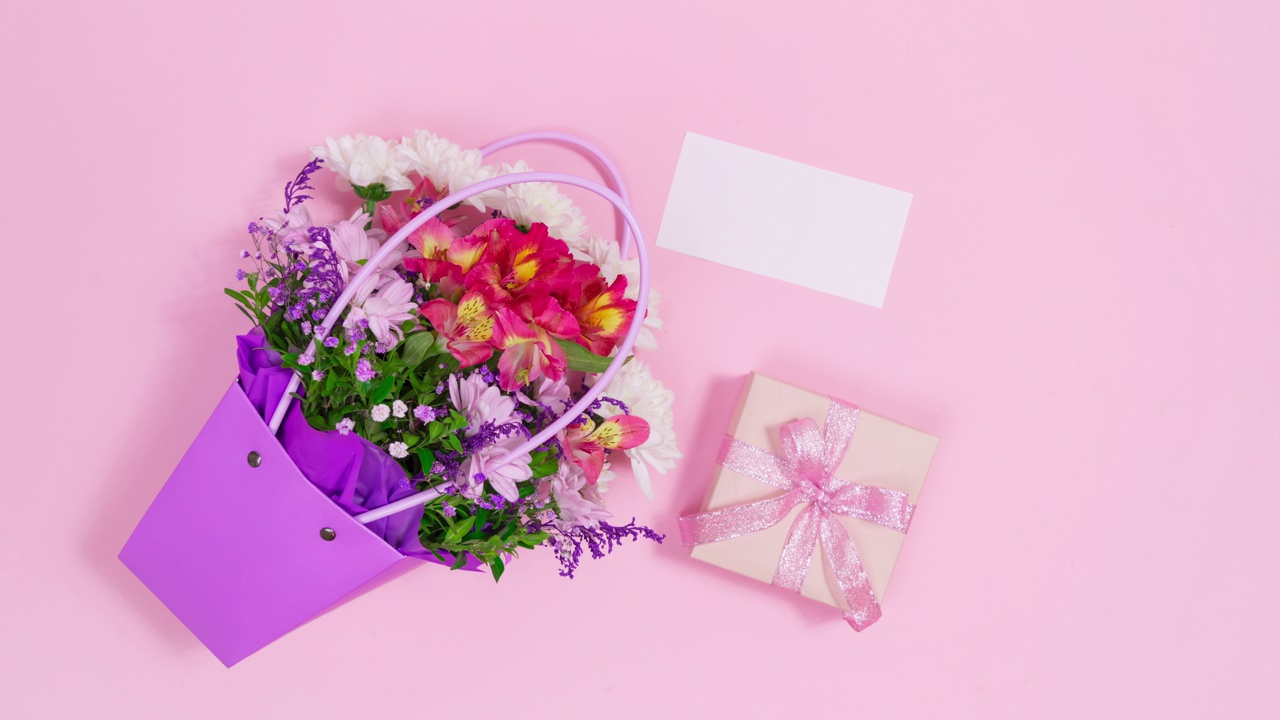 一束鲜花在紫色的袋子连同白色的卡片和礼盒出现在粉红色的背景。视频下载