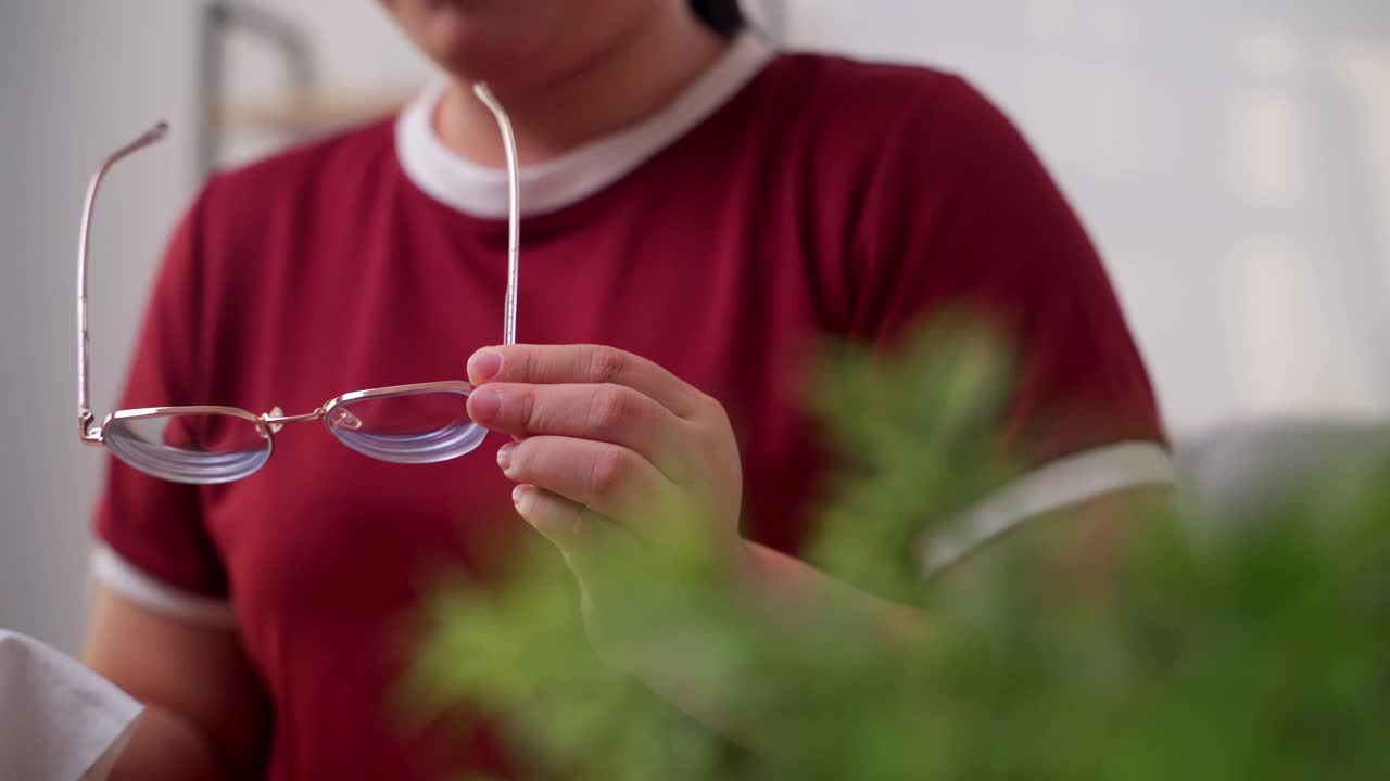 这位女士坐在家里的客厅里，正在用超细纤维布擦拭他的眼镜。视频下载