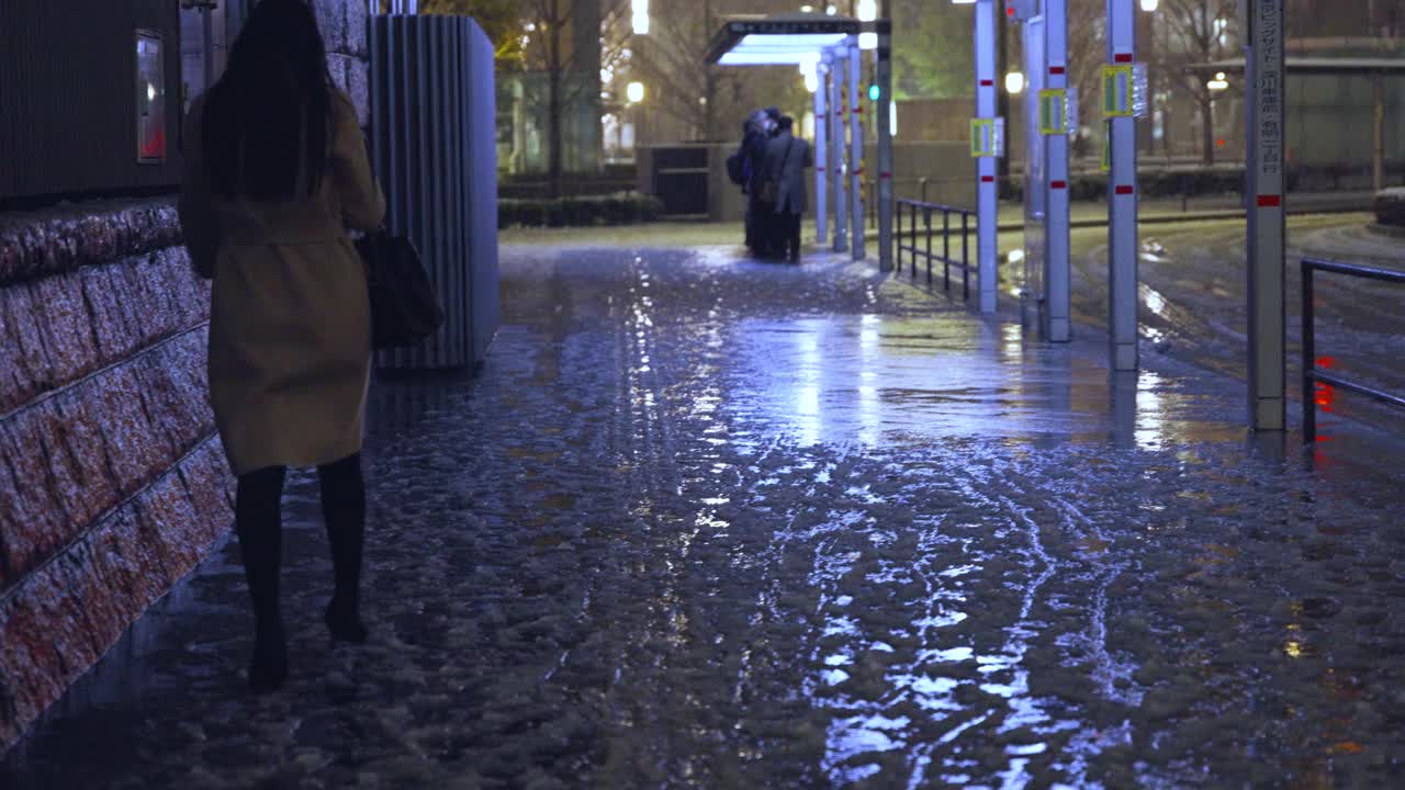 东京晚上下着雨夹雪，一名女行人独自走在丸之内的夜间街道上视频素材