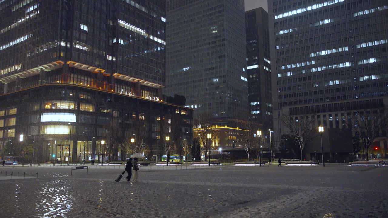 夜晚，东京的摩天大楼上飘着雪花，丸之内的行人打着伞行走视频素材