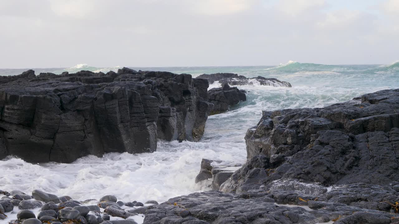 海浪拍打着冰岛的黑色玄武岩海岸，多云的天空，充满活力的海洋景象视频素材