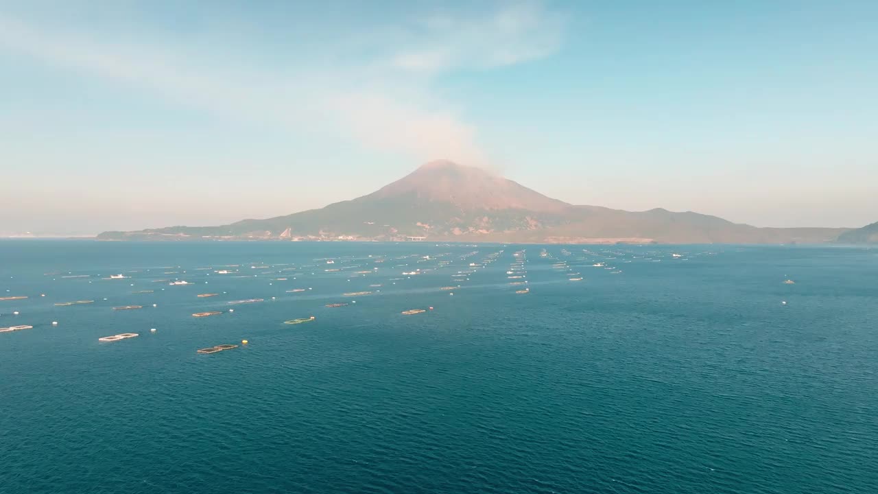 在阳光明媚的日子里，一艘渔船驶向鹿儿岛湾蔚蓝的海水和冒着烟的樱岛火山视频素材