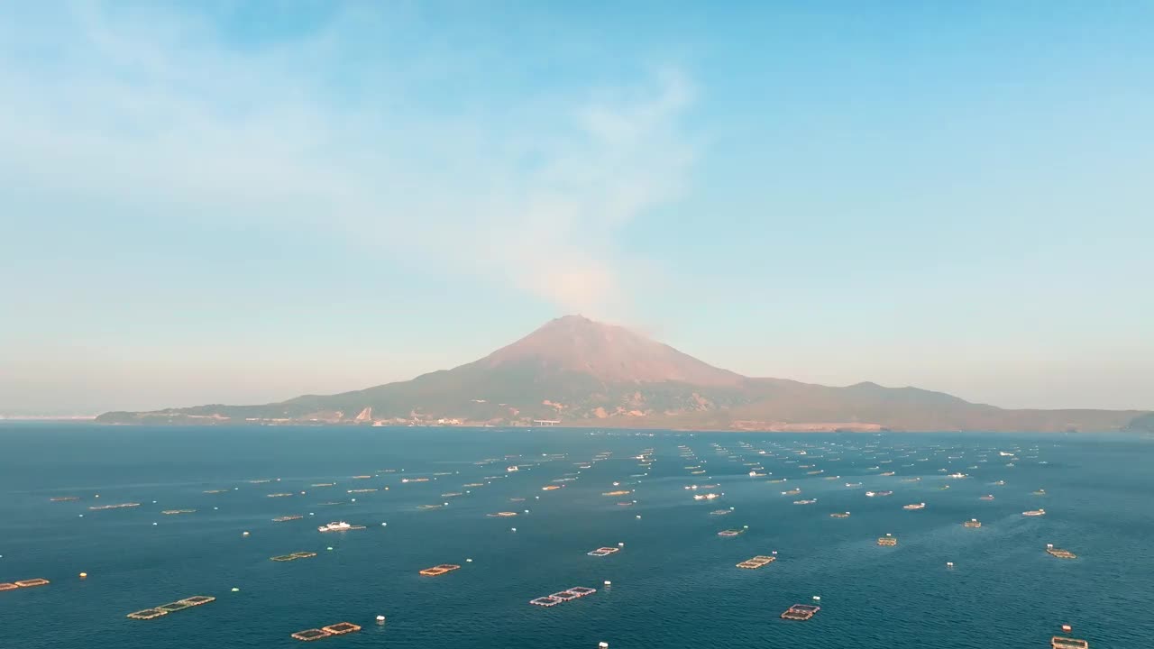 在阳光明媚的日子鸟瞰鹿儿岛湾的蓝色大海和樱岛火山下的许多养鱼场视频素材