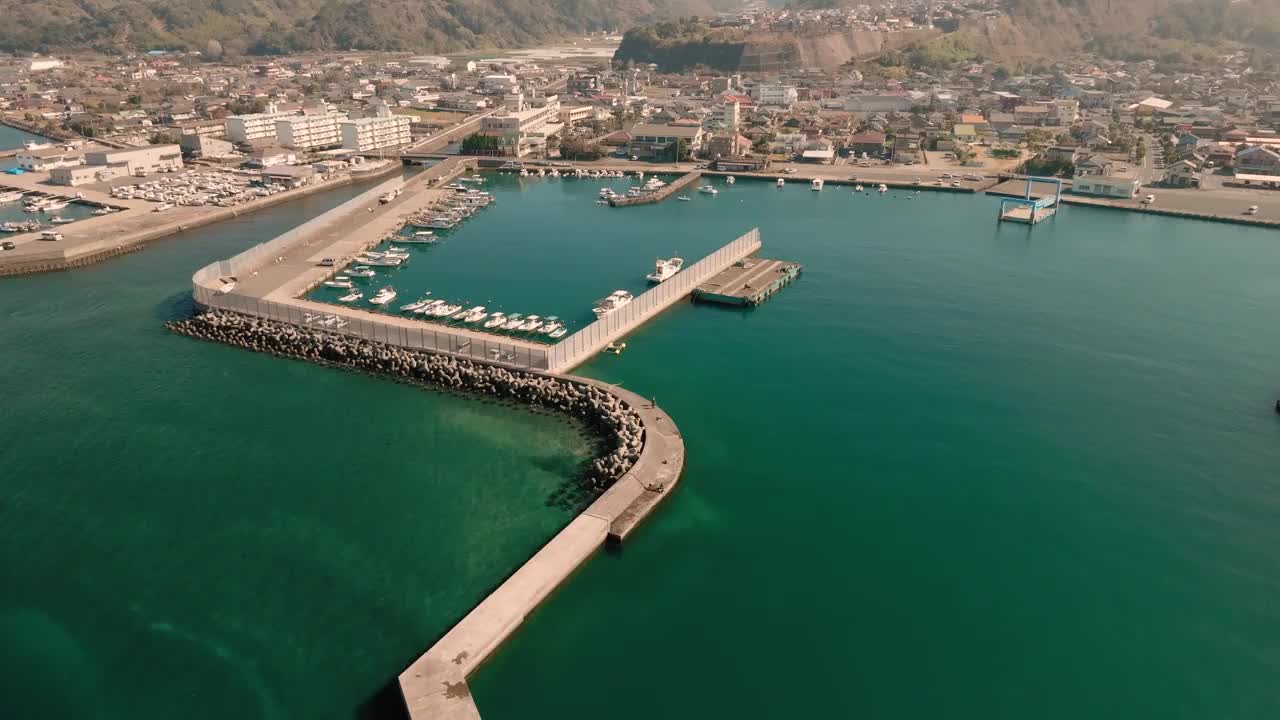 蔚蓝的大海和一个小渔港的堤岸鸟瞰图，在一个阳光明媚的日子里，渔船停泊在那里视频素材