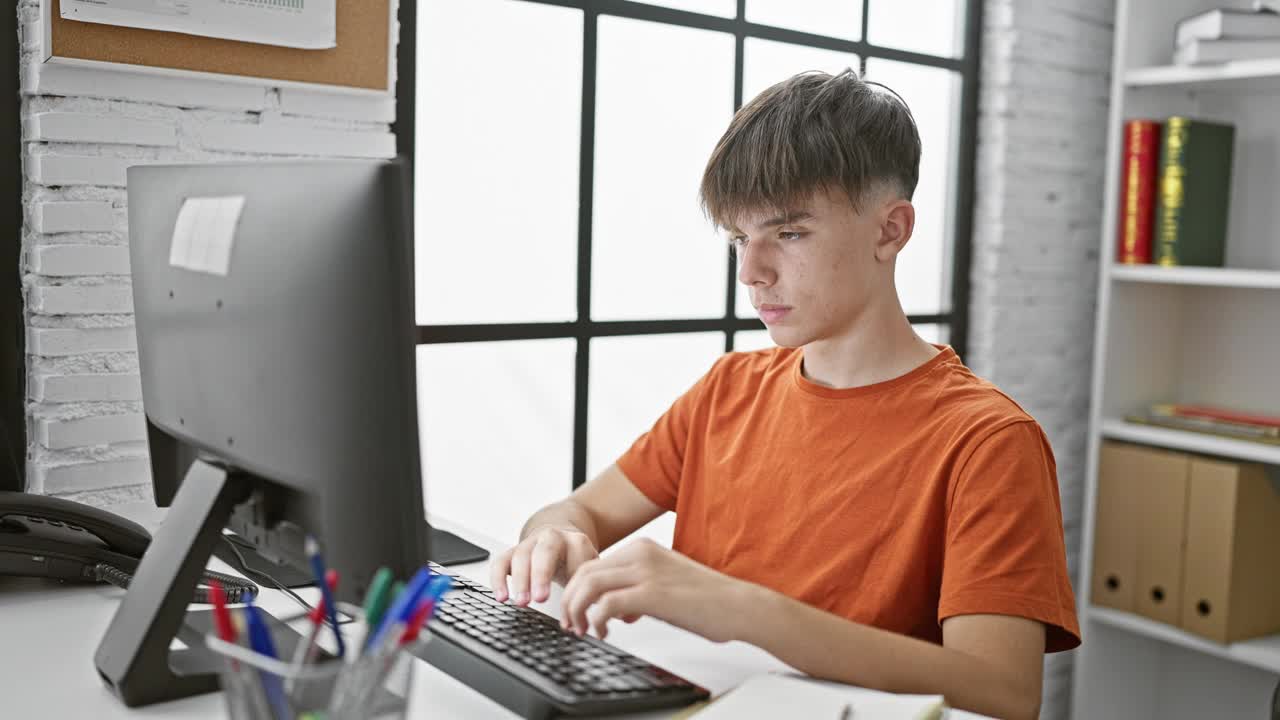 一个穿着橙色衬衫的年轻白人男性少年在现代图书馆的电脑前学习和放松。视频素材