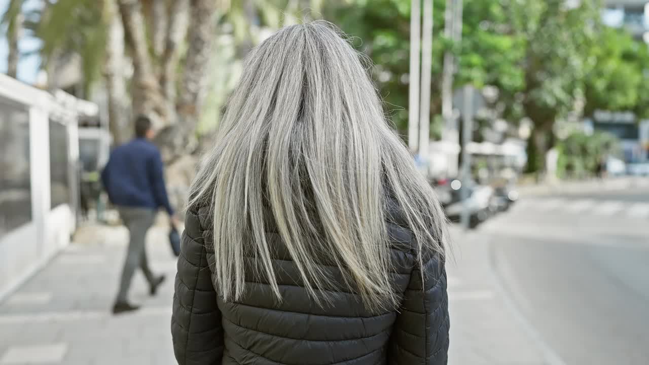 白发苍苍的成熟女子在城市街头自信地微笑着，演绎着随意的都市生活方式。视频素材