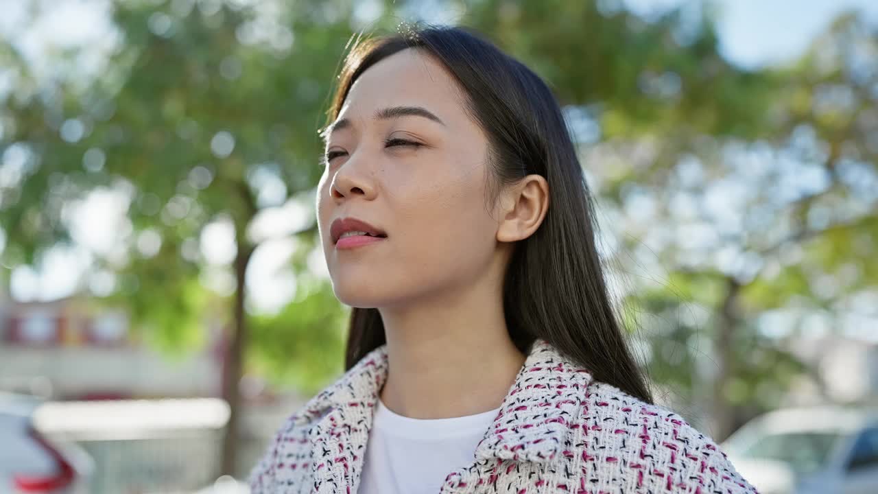 一位宁静的年轻亚洲女子在阳光明媚的城市街道上享受着户外的宁静时光。视频素材