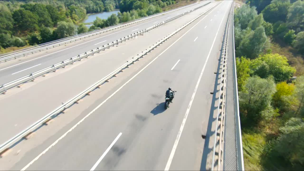 夏日，骑摩托车的人在公路旅行中驾驶摩托车。男子在高速公路上快速骑着现代运动摩托车。摩托车手在乡间小路上飙车。冒险的概念。空中拍摄视频素材