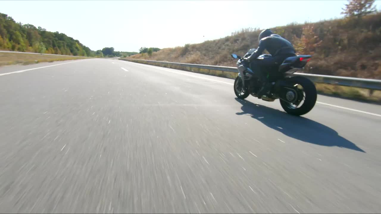 夏日，骑摩托车的人在公路旅行中驾驶摩托车。男子在高速公路上快速骑着现代运动摩托车。摩托车手在乡间小路上飙车。冒险的概念。空中拍摄视频素材