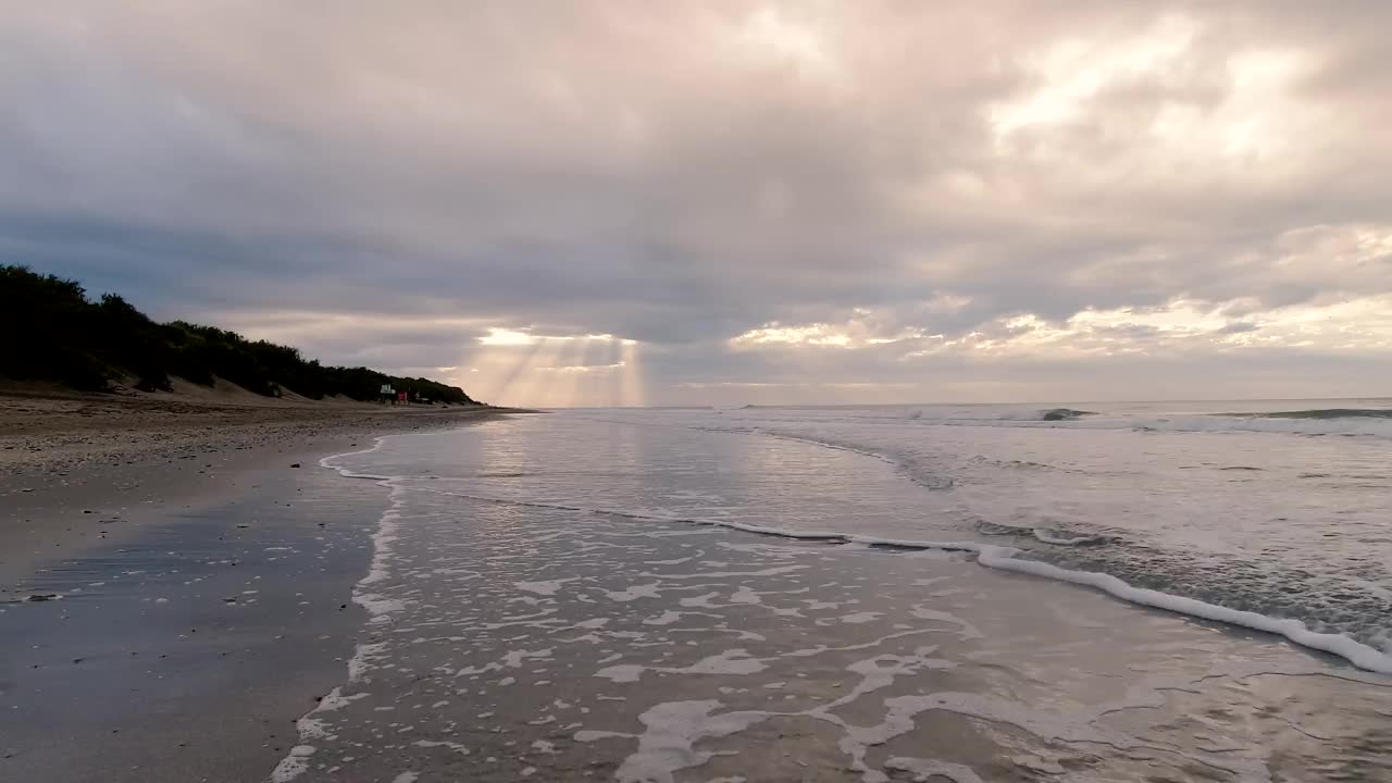 沙滩上的黎明，阳光透过云层，柔和的海浪反射着湿润的沙滩视频下载