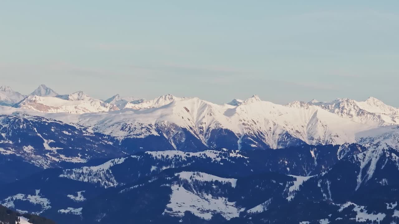 空中无人机拍摄的日出时白雪覆盖的山脉的剪影。视频素材