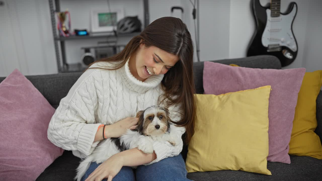 一个微笑的女人抱着她的猎犬坐在舒适的沙发上，沙发上有彩色的靠垫。视频素材