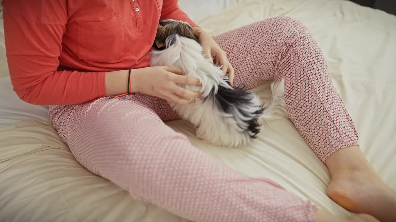 在一间舒适的卧室里，一名女子在床上拥抱着她的小猎犬，传达出一种在家的陪伴和舒适感。视频素材