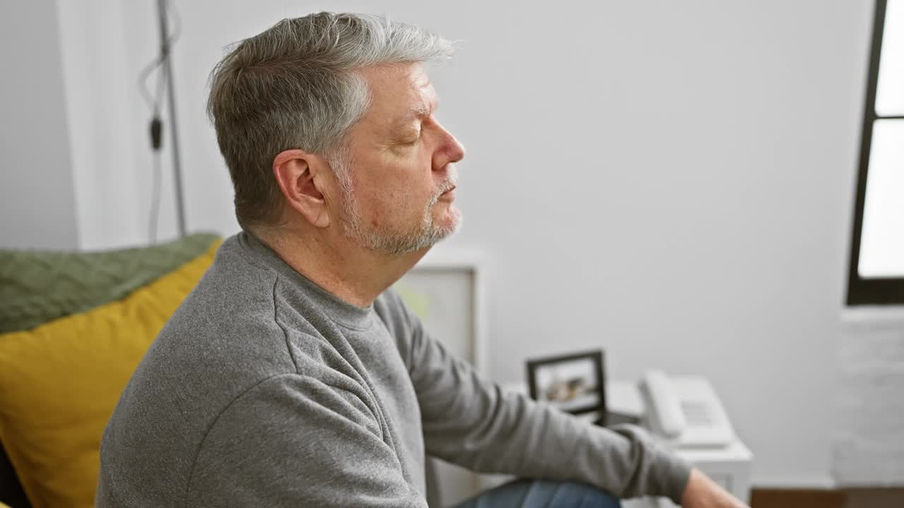 在一个舒适的家庭室内，一个安详、白发苍苍的男人躺在沙发上，沙发上有五颜六色的靠垫。视频素材