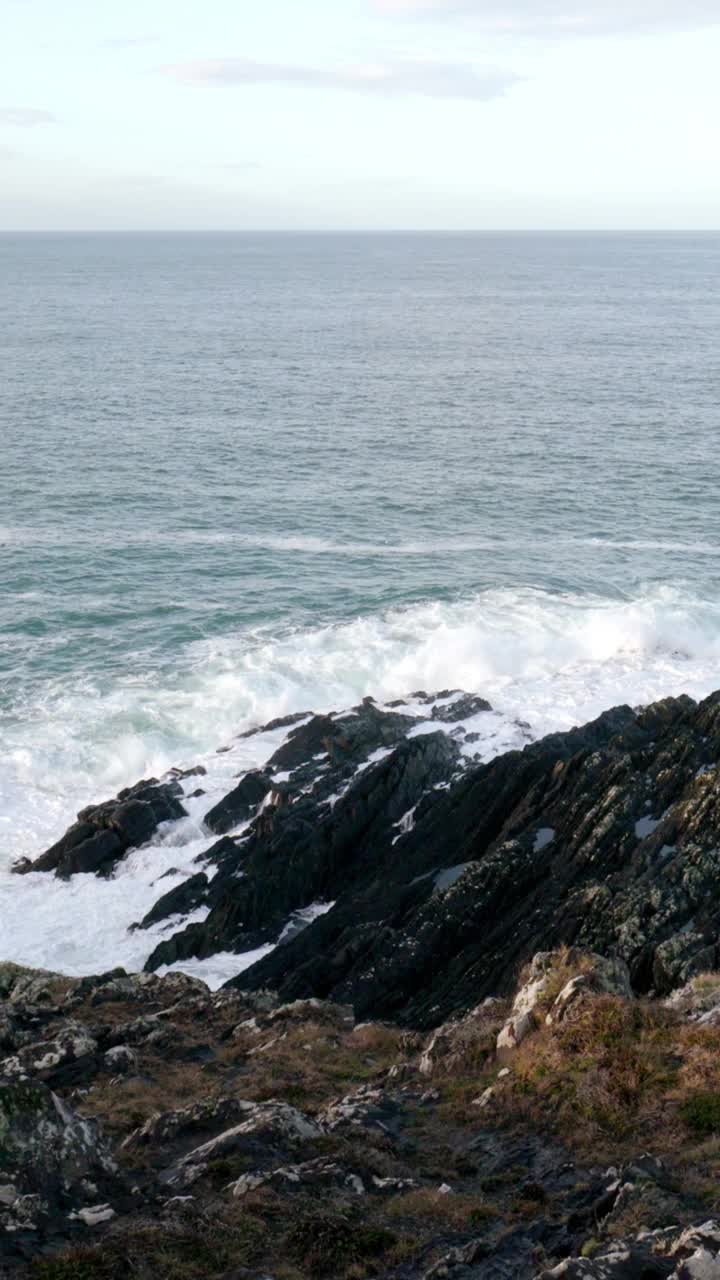 岩石嶙峋的海岸线，锯齿状的岩石在无情的海浪中屹立不倒。深蓝色的大海和白色的浪花。垂直视频，平移。视频素材