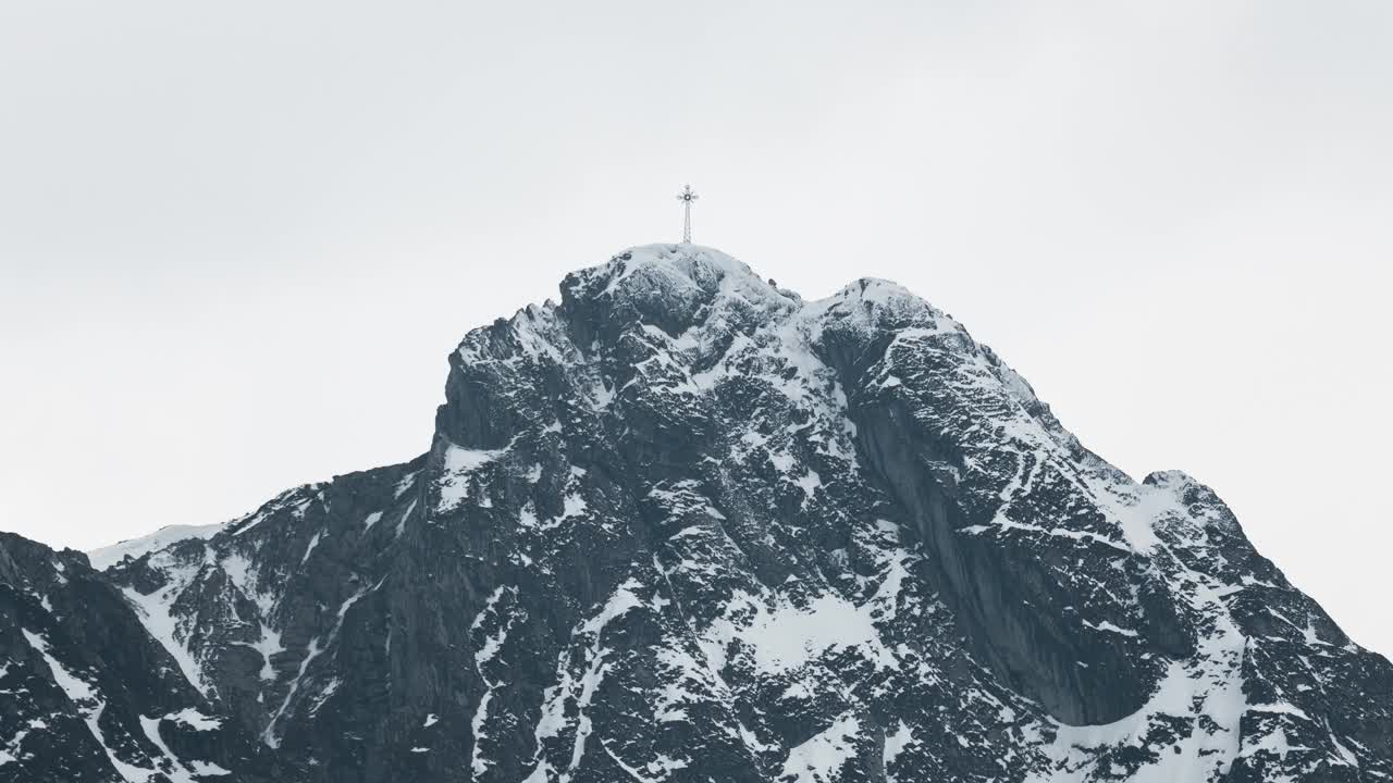 山顶:被雪覆盖的岩石山顶，可以看到一群登山者或徒步旅行者的剪影山顶上有一个巨大的金属十字架。视频素材