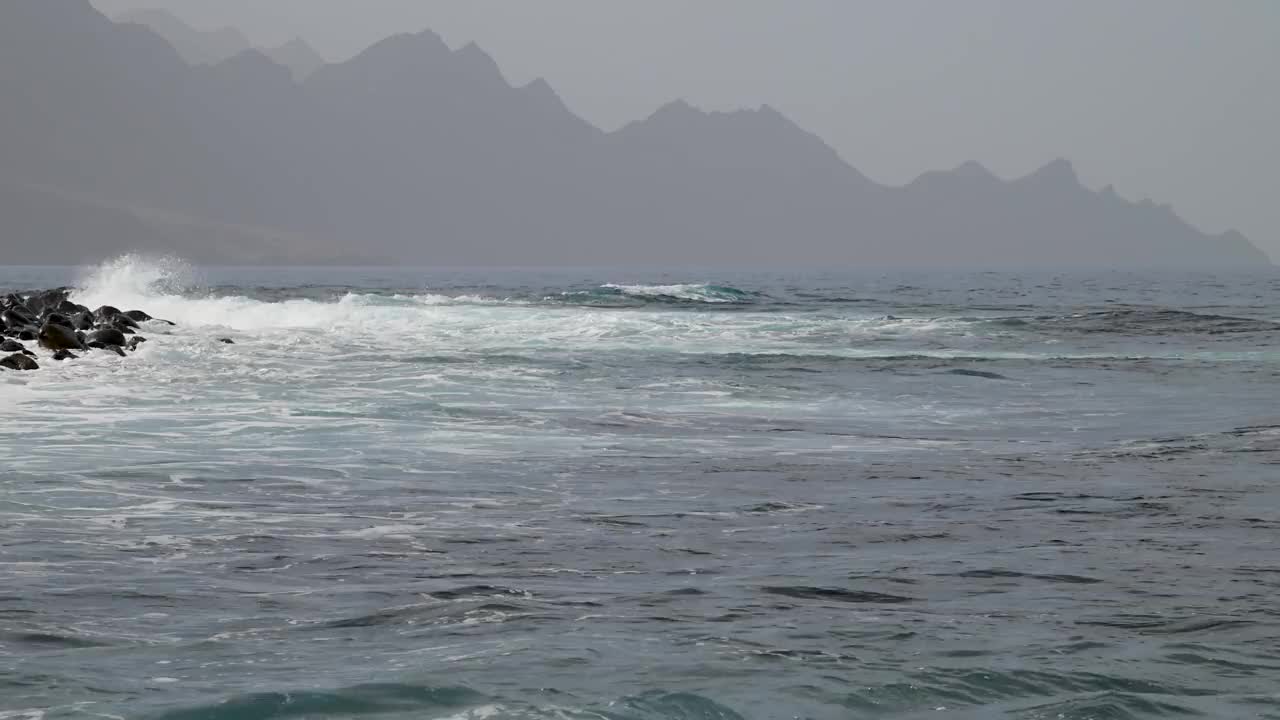 海浪在阿加埃特海岸附近破碎，背景是大加那利岛西部山脉的“龙尾”。视频素材