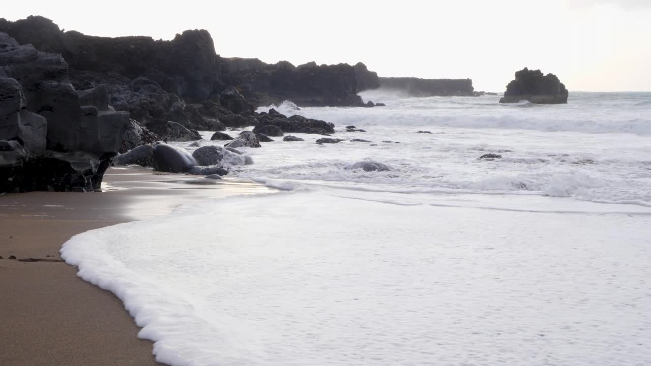 黄昏时分，柔和的海浪冲刷着黑色的沙滩和火山玄武岩视频素材