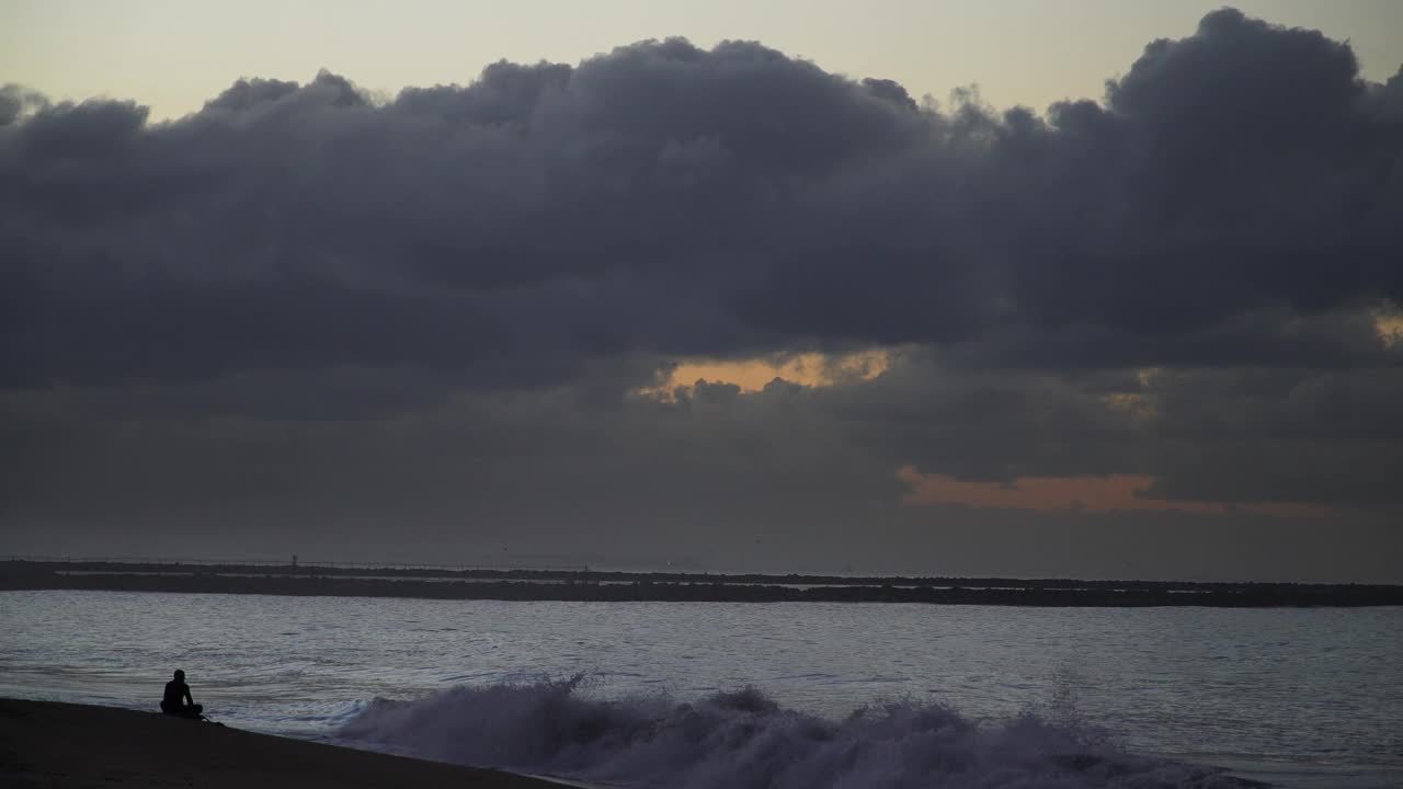 一个人在黄昏的海豹海滩上，地平线上乌云密布，宁静的海洋景象视频素材