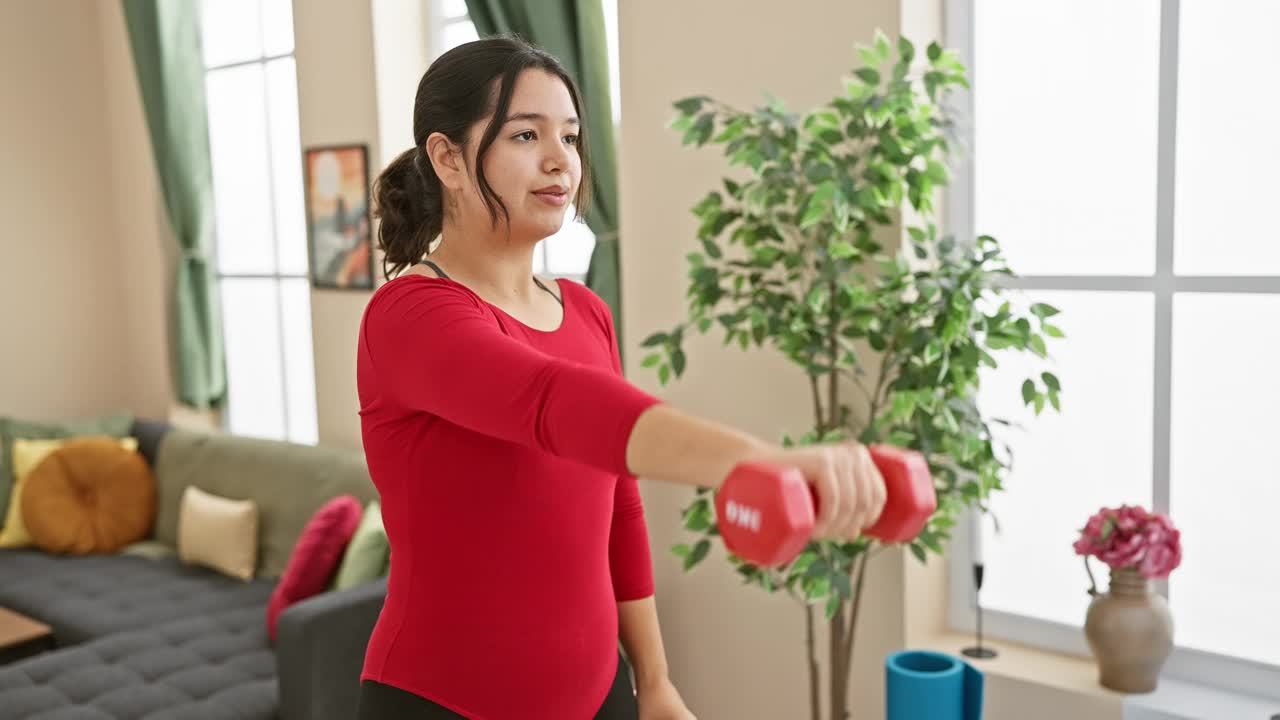 一位年轻的西班牙妇女在她现代的客厅里用哑铃练习，专注而沉着。视频素材