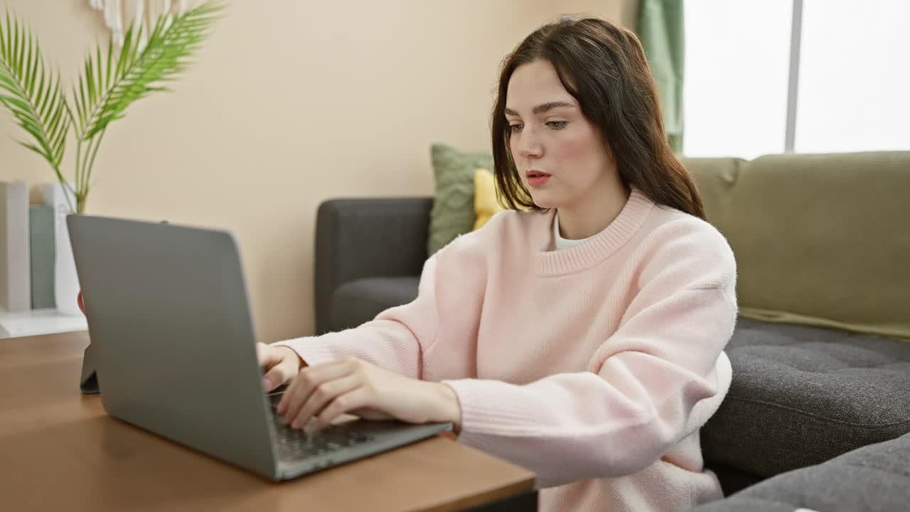 一名年轻女子在家里做多件事，在舒适的客厅里使用笔记本电脑和智能手机。视频素材