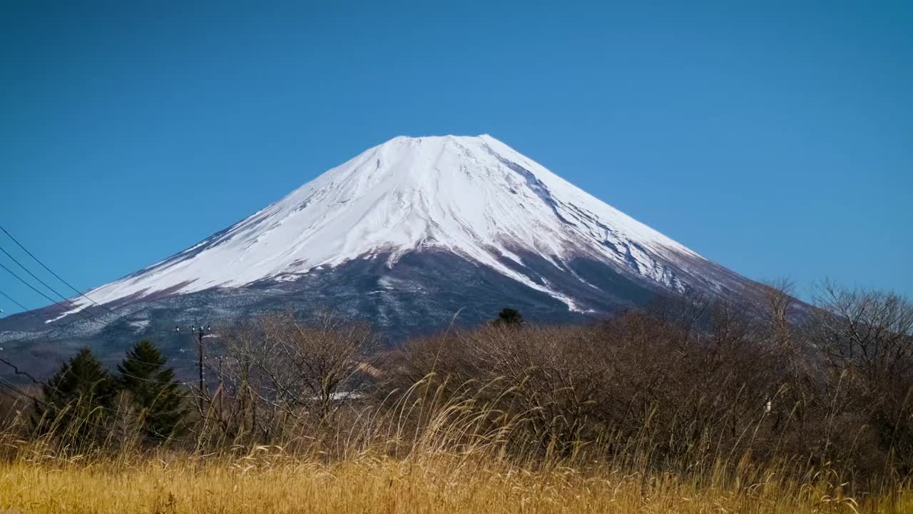 在蓝天的日子里，富士山映衬着群山和草地，是游客和旅行者的地标和目的地。大自然的美在平和中伴着缓慢的冬天的风视频下载