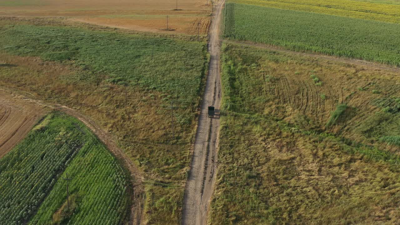 夏日里，农用拖拉机拖着空货车行驶在乡间的土路上，在地上投下阴影，无人机拍摄的航拍画面视频素材