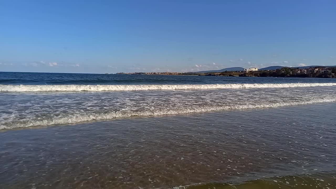 阳光明媚的夏日，风景如画的海景。小波浪拍打着海岸，山脉和度假小镇在地平线上清晰可见。在保加利亚黑海海岸度假，Kiten镇，南海滩视频素材