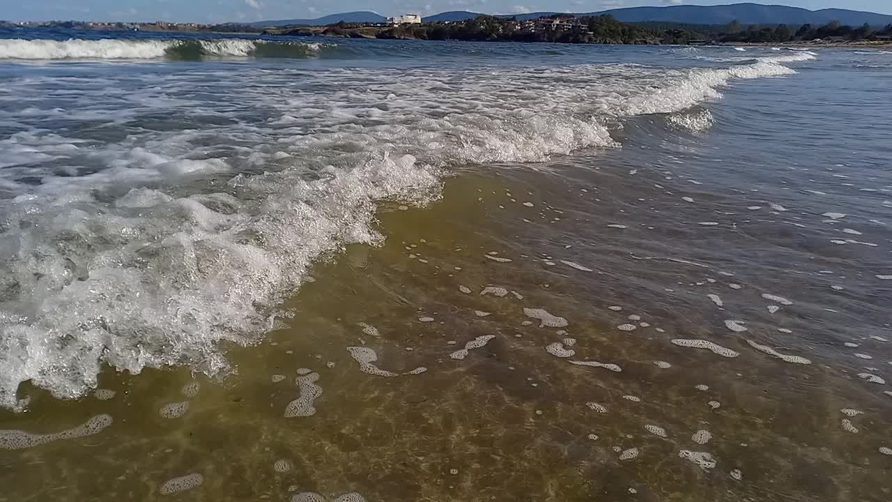 阳光明媚的夏日，风景如画的海景。小波浪拍打着海岸，山脉和度假小镇在地平线上清晰可见。在保加利亚黑海海岸度假，Kiten镇，南海滩视频下载