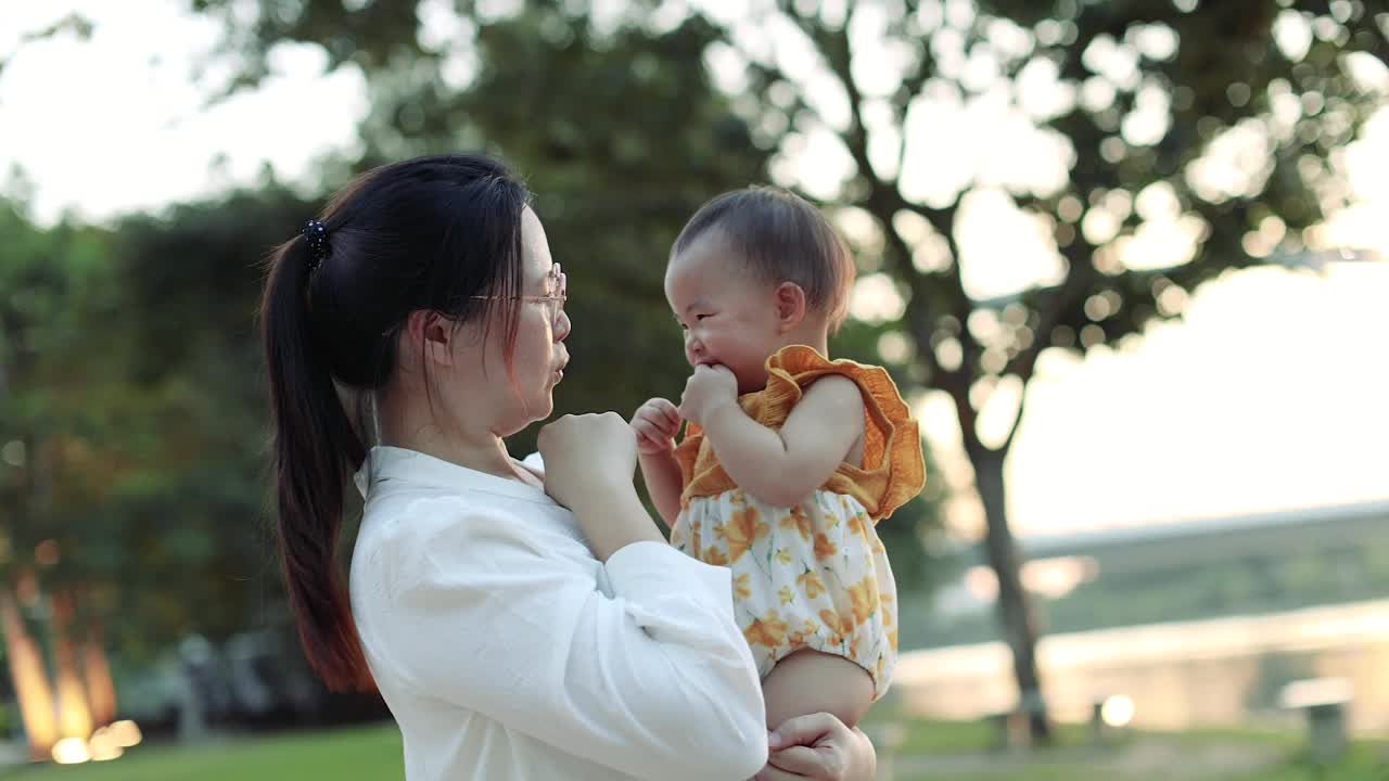 一位亚洲母亲在花园公园里给她的女婴挠痒痒，并和她击掌。股票视频视频素材