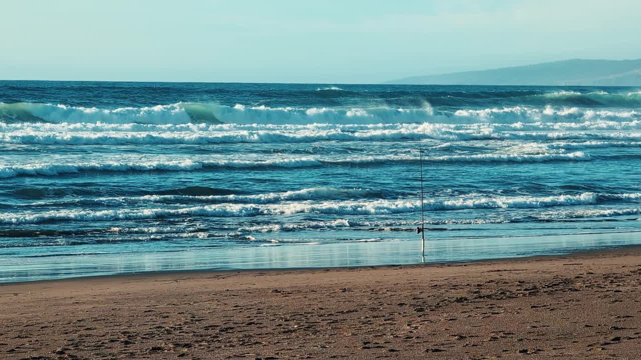 在一个阳光明媚的日子里，用鱼钩在海滩上拍摄蓝色海浪的慢动作视频素材