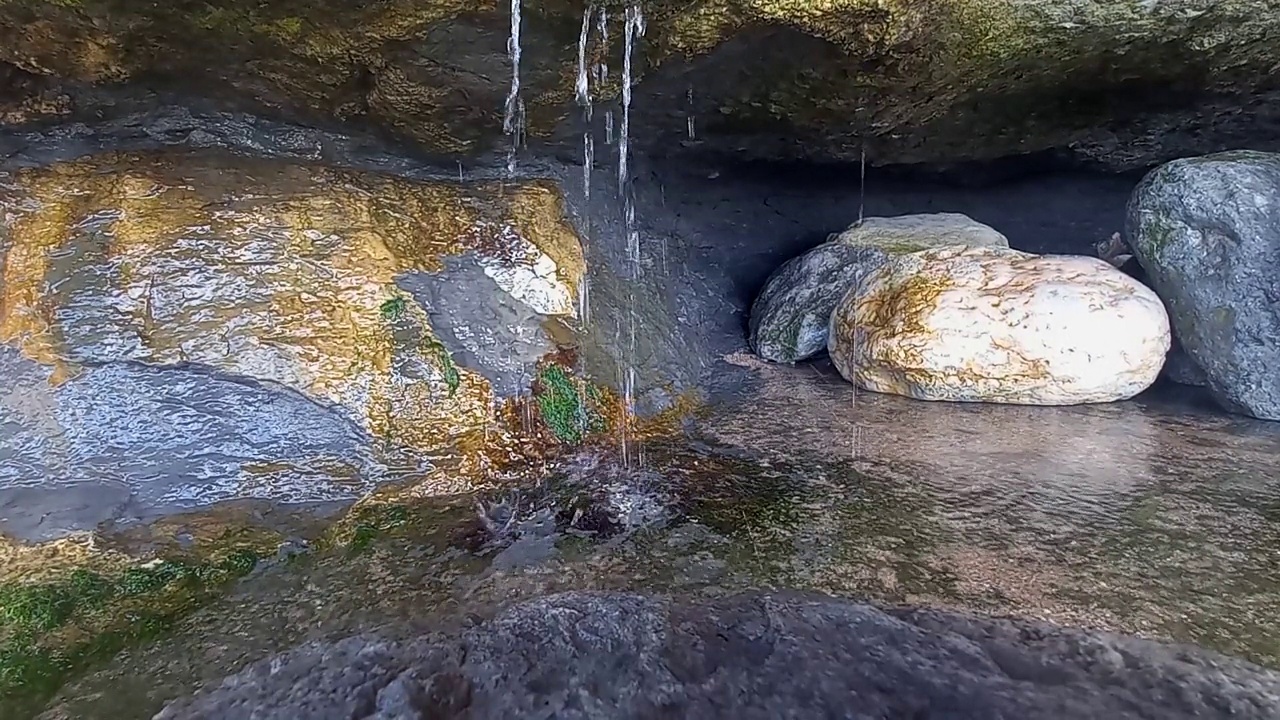 清澈的水从靠近大海的山坡上洞穴的岩石中流下来视频素材