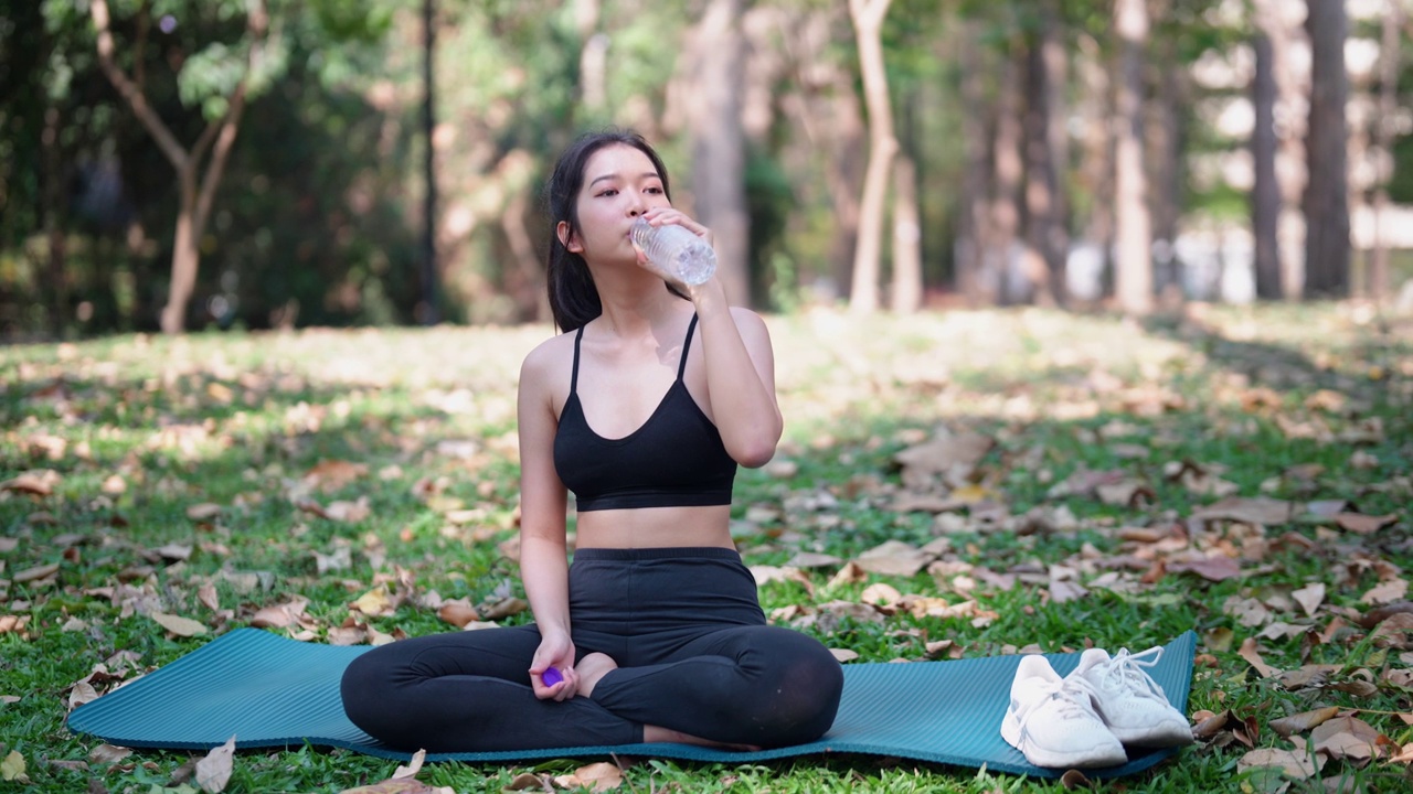 穿着运动服的亚洲女运动员，在运动休息时用瓶装水补水，在公园里优先考虑补水和健康视频素材