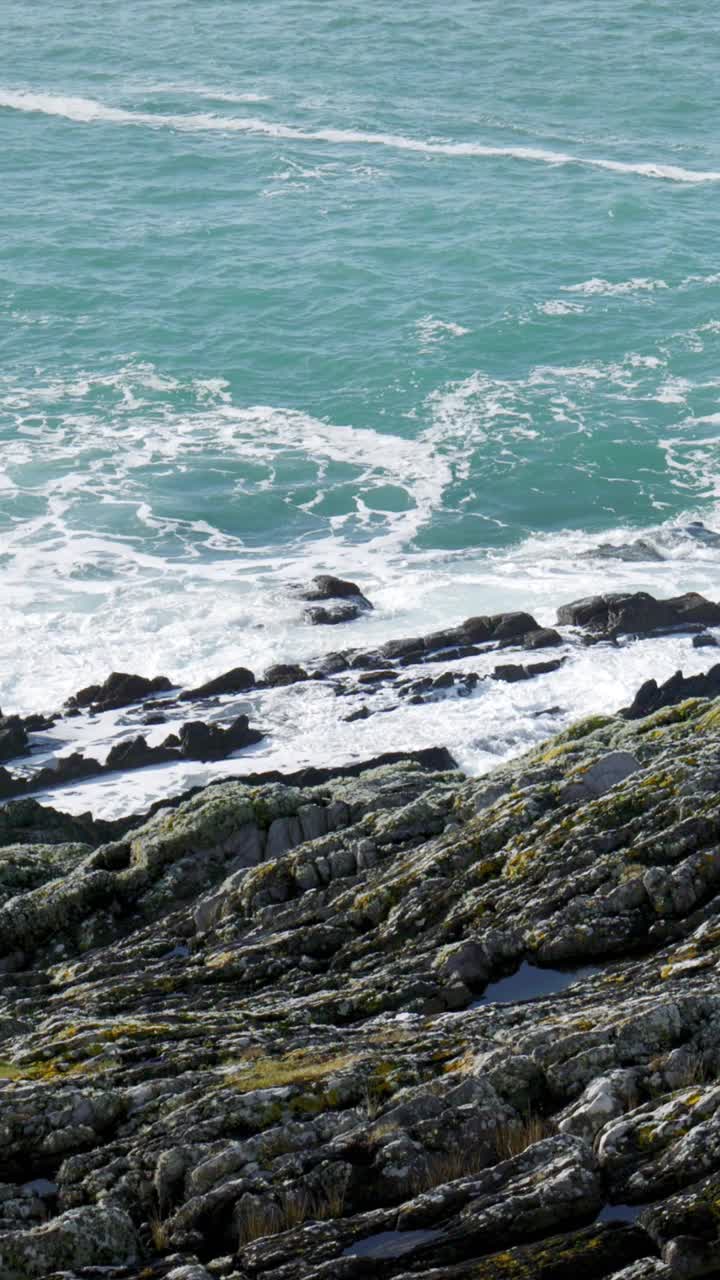 岩石嶙峋的海岸线，漆黑嶙峋的岩石承受着无情海浪的冲击。垂直视频。视频素材