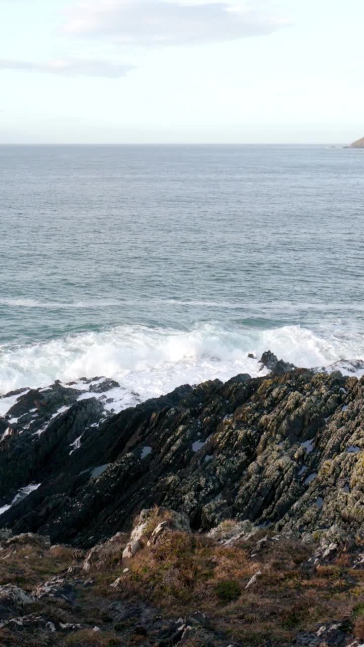 锯齿状的岩石勾勒出海岸线，海浪。深蓝色的大海，而白色的泡沫从海浪增加了一种动感的场景。垂直视频。视频素材